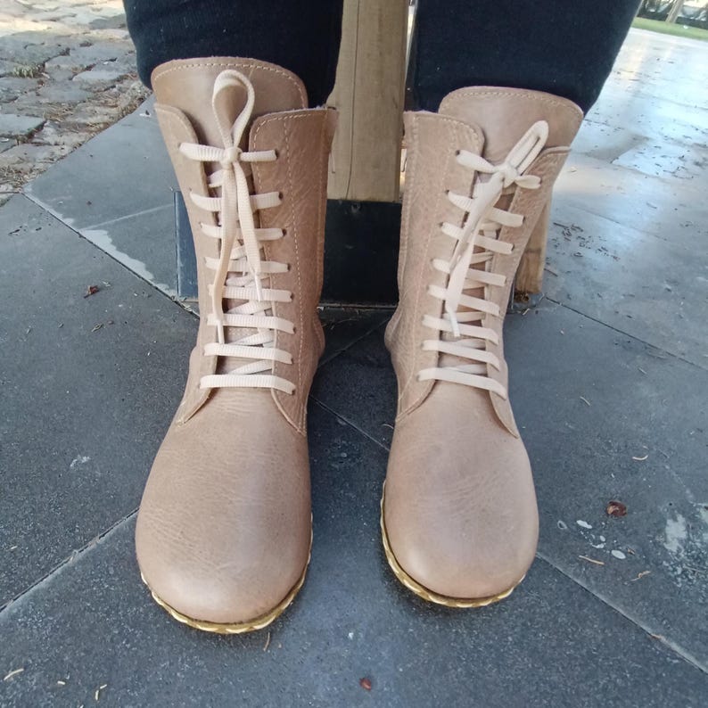 May include: A pair of light brown leather boots with white laces. The boots have a rounded toe and a low heel.