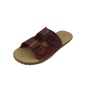 May include: A pair of brown leather sandals with two adjustable straps and metal buckles. The sandals have a light-colored footbed and are stitched around the edges. The footwear is designed for casual wear.