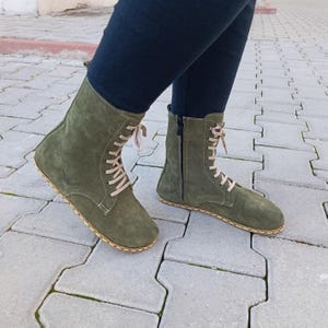 Peut inclure: Une paire de bottines en daim vert olive à lacets et fermeture éclair sur le côté. Les bottes ont une semelle plate et un bord cousu.