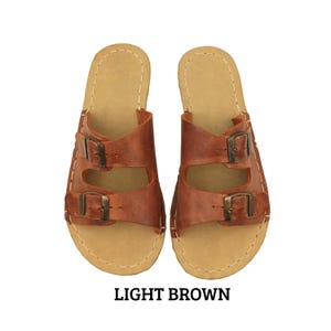 May include: Light brown leather sandals with two buckle straps. The sandals have a light tan footbed and are stitched with white thread. The text "LIGHT BROWN" is displayed below the sandals.