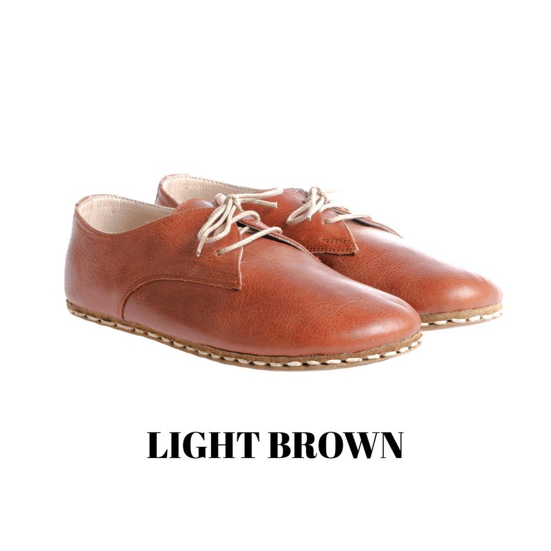 May include: A pair of light brown leather shoes with a rounded toe, low-cut silhouette, and thin cream-coloured laces. The shoes feature visible stitching along the sole and the text LIGHT BROWN is printed in black below the footwear.
