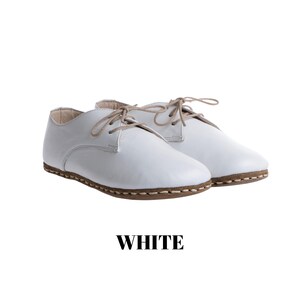 May include: A pair of white leather lace-up shoes featuring a rounded toe, beige laces, and a visible brown stitched welt along the sole. The word WHITE is printed in bold black capital letters below the shoes on a plain white background.