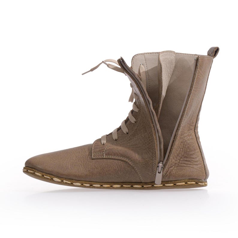 May include: A pair of beige leather ankle boots with a side zip and laces up the front. The boots have a flat sole and a rounded toe.