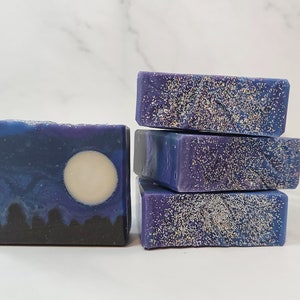 May include: Four bars of handmade soap, one with a moon design and three with a glittery purple and blue design.
