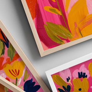 Peut inclure: Gros plan sur des impressions d'art floral encadr&eacute;es. Les peintures pr&eacute;sentent des coups de pinceau vibrants dans des tons roses, jaunes, oranges et bleus. Les cadres sont en bois naturel ou blancs, cr&eacute;ant une esth&eacute;tique moderne. L'&oelig;uvre repr&eacute;sente des fleurs abstraites.