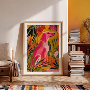 Peut inclure: Une impression encadr&eacute;e d'art repr&eacute;sentant un chien rose assis au milieu d'un feuillage color&eacute;. L'&oelig;uvre d'art pr&eacute;sente une palette vibrante de rose, de jaune, d'orange et de vert. L'impression est encadr&eacute;e dans un cadre en bois clair.