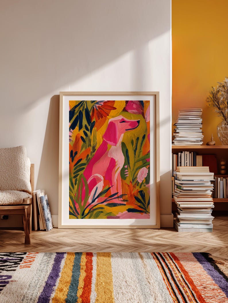 Peut inclure: Une impression encadr&eacute;e d'art repr&eacute;sentant un chien rose assis au milieu d'un feuillage color&eacute;. L'&oelig;uvre d'art pr&eacute;sente une palette vibrante de rose, de jaune, d'orange et de vert. L'impression est encadr&eacute;e dans un cadre en bois clair.