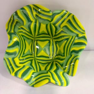 May include: A decorative glass bowl with a unique, swirled pattern of yellow and green. The bowl has an organic, free-form shape with a textured interior. The colors blend together, creating a vibrant and eye-catching design.