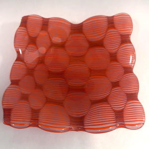 Peut inclure: Un plat décoratif en verre avec un bord ondulé. Le plat présente un motif de cercles rayés orange et blancs, créant un effet de bulles. Les couleurs sont vives et le design est attrayant.