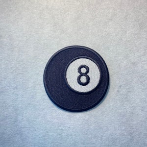 Könnte beinhalten: Ein gestickter Patch einer Billardkugel mit der Nummer 8 in Schwarz und Weiß.