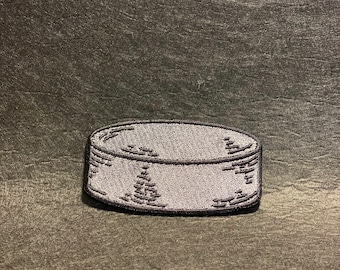 May include: A grey embroidered patch shaped like a drum with black stitching.