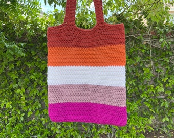 May include: A crocheted tote bag with a striped design in shades of red, orange, white, pink, and magenta. The bag has two long straps.