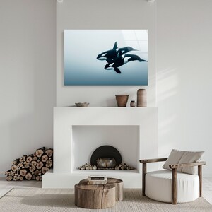 Puede incluir: Una impresi&oacute;n enmarcada de tres orcas blancas y negras nadando en un oc&eacute;ano azul. La impresi&oacute;n est&aacute; colgada en una pared blanca sobre una chimenea.