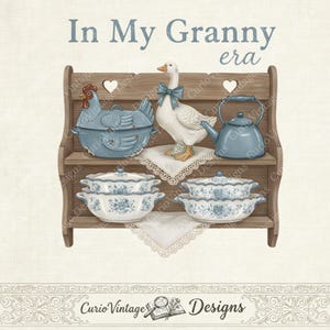 Op de afbeelding: Een vintage illustratie met een houten plank met blauw en wit keramisch keukengerei. De plank bevat een blauwe kipvormige ovenschaal, een witte gans met een blauwe strik en een blauwe theepot. De tekst "In My Granny era" staat bovenaan.