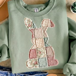 Puede incluir: Sudadera verde salvia con un dise&ntilde;o de conejo de patchwork. El conejo est&aacute; compuesto por varios patrones de tela, incluyendo estampados florales, a rayas y a cuadros en tonos rosa, crema y azul. La sudadera tiene cuello redondo y mangas largas.