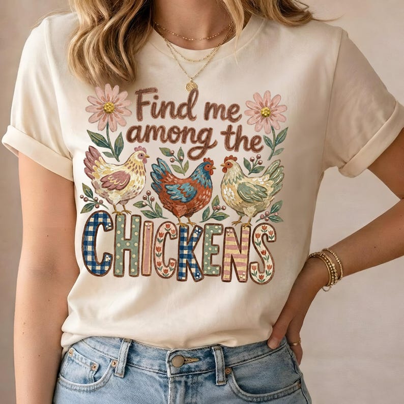 May include: Cream-colored t-shirt featuring a whimsical design with three chickens and floral accents. The text "Find me among the Chickens" is displayed in a decorative font, making it a charming addition to any wardrobe.