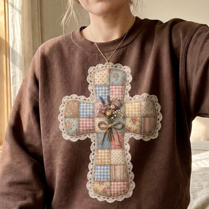 Puede incluir: Una sudadera marr&oacute;n con un gran colgante de cruz. La cruz est&aacute; adornada con patrones florales y a cuadros, un ribete de encaje y un peque&ntilde;o ramo de flores secas. El colgante cuelga de una delicada cadena dorada.