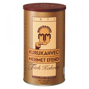Peut inclure: Une boîte de café turc de couleur marron et or avec le nom de la marque "Kurukahveci Mehmet Efendi" et le texte "Turk Kahvesi" imprimé sur le devant. La boîte a un couvercle rouge et un poids net de 500 grammes.