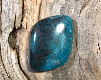 May include: A smooth, polished turquoise cabochon with a dark blue and green color. The stone has a mottled pattern with black and brown inclusions.