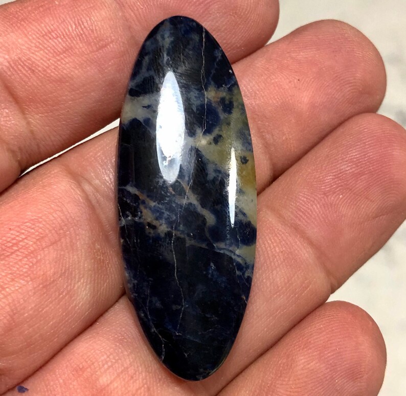 Puede incluir: Un cabuj&oacute;n liso de forma ovalada de sodalita azul y blanca con un patr&oacute;n de m&aacute;rmol azul oscuro y blanco.