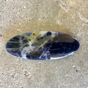 Puede incluir: Una piedra lisa de forma ovalada con un patr&oacute;n de m&aacute;rmol azul, blanco y amarillo.