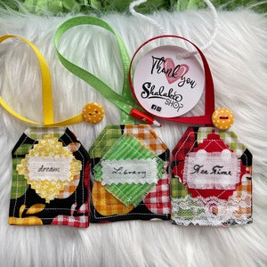 May include: Three fabric gift tags with black and white gingham, red and white gingham, and black and white gingham with lace trim. The tags are decorated with fabric scraps and have the words "dream", "library", and "tea time" written on them.