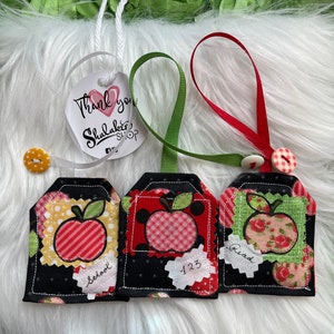May include: Three black fabric gift tags with red apple designs. The tags are decorated with different patterns and have the words "School", "123", and "Read" written on them.