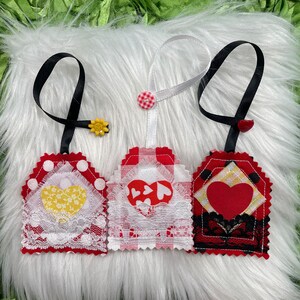 May include: Three red and white fabric gift tags with heart designs. The tags are attached to black and white ribbon.