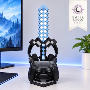 May include: A black gaming controller and headset stand featuring a vertical pixelated sword design in shades of light and dark blue. The stand is constructed with a base that holds the controller and a central pillar that supports the headset.