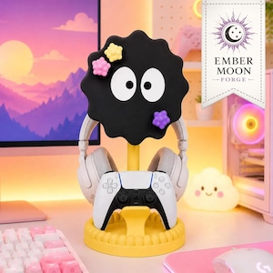 Può includere: Un supporto giallo per cuffie e controller con una testa di personaggio nera e circolare, due grandi occhi bianchi e tre piccoli accenti colorati a forma di stella. Il supporto include una base rotonda e un montante centrale.