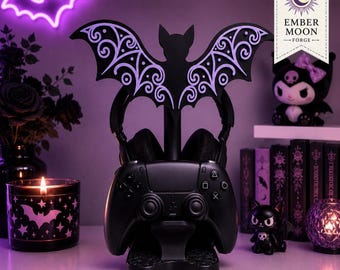 May include: A black gaming controller and headset stand featuring a large, decorative bat silhouette with intricate purple scrollwork patterns on its wings. The stand is designed to hold a black game controller in the front and a headset above.