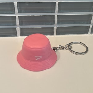 May include: Pink bucket hat keychain with a white Reebok logo.