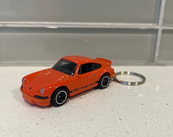 May include: Orange toy car keychain with black racing stripes. The car is a Porsche 911.