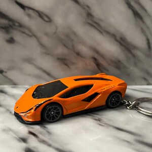 Può includere: Macchinina giocattolo Lamborghini arancione con ruote nere e un portachiavi argentato.