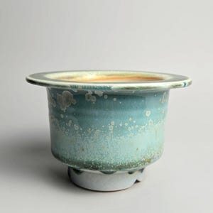 Peut inclure: Un bol en céramique avec un bord large et plat et une base effilée. L'extérieur présente un vernis dégradé passant d'un bleu sarcelle profond en haut à un vert menthe clair et tacheté en bas. L'intérieur a une teinte orange clair et chaude.