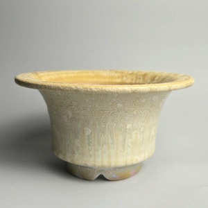 Peut inclure: Un bol en céramique avec un bord large et évasé et un corps effilé. L'extérieur présente un vernis moucheté jaune pâle et crème avec une texture cristalline subtile et des motifs de gouttes verticaux. La base a un petit pied cranté.