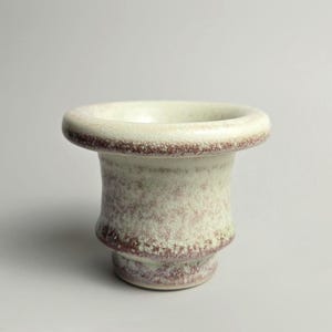 Könnte beinhalten: Ein Keramikgefäß mit einem breiten, abgerundeten Rand und einem sich verjüngenden Körper. Die Oberfläche weist eine gesprenkelte, melierte Glasur in Off-White, Creme und Rotbraun auf, die ein strukturiertes Erscheinungsbild erzeugt.