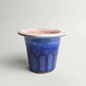 Peut inclure: Un pot en céramique avec un large bord plat présentant un émail rose et blanc. Le corps du récipient est d'un bleu profond et vibrant avec une finition brillante et des motifs de gouttes bleu foncé descendant le long des parois.
