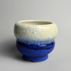 May include: A set of three ceramic mugs with a speckled, matte finish. Each mug features a different color: light blue, cream, and gray. The mugs have a simple, modern design, suitable for coffee or tea.