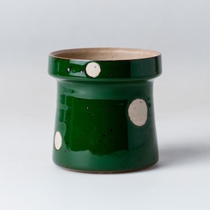 May include: A green ceramic planter with white polka dots. The planter has a wide base and a narrow top.