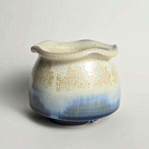 May include: A white ceramic pot with a wavy rim and a blue and gold glaze. The pot is handmade and has a unique, organic shape.