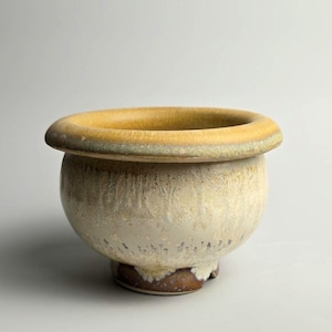 May include: A ceramic bowl with a wide, yellow rim and a rounded body. The bowl has a textured, off-white exterior with a brown base. The design is simple and elegant, suitable for various decorative purposes.