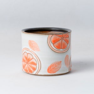 May include: White ceramic planter with a black rim and orange citrus fruit and leaf designs.