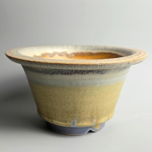 Könnte beinhalten: Ein Keramik-Pflanztopf mit breitem, ausgestelltem Rand und rundem Boden. Die Außenseite weist einen Farbverlauf auf, darunter Gelb, Blau und Braun. Der Topf ist für die Aufnahme von Pflanzen konzipiert und verleiht jedem Raum eine dekorative Note.