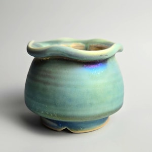 Peut inclure: Un petit pot en céramique bleu et vert avec un bord ondulé. Le pot a un glaçage iridescent.