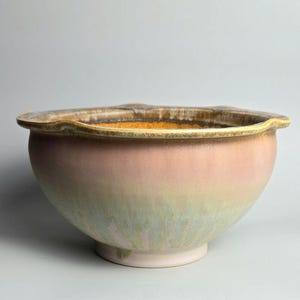 Peut inclure: Un bol en céramique avec un large bord festonné. Le bol présente un dégradé de rose et de vert avec un bord marron. Le bol est rond et repose sur une petite base ronde.