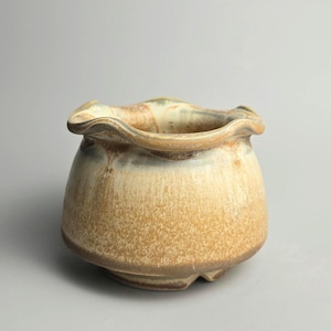 May include: A handmade ceramic bowl with a wavy edge. The bowl has a speckled, earthy colour scheme of tan, brown, and cream. The rounded shape and textured surface give it a rustic, artisanal feel. Suitable for serving or as a decorative item.