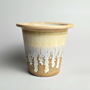 May include: A ceramic plant pot with a wide rim and a cylindrical body. The exterior has a gradient of colours, changing from a light tan at the top to a creamy white with brown accents at the bottom. Suitable for indoor or outdoor use.