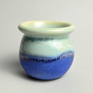 May include: A small, round ceramic pot with a light blue, white, and dark blue glaze. The pot is ideal for small plants or succulents.