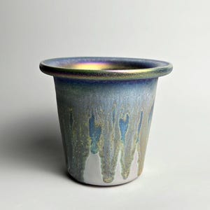 May include: A handmade ceramic vase with a flared rim. The vase has a blue and green iridescent glaze that drips down the sides. The interior rim has a gold-coloured sheen.